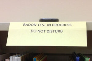 Radon measurement device on shelf in school library with sign saying Radon Test in Progress, Do Not Disturb