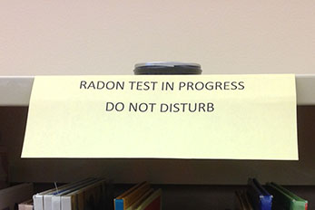 Radon measurement device on shelf in school library with sign saying Radon Test in Progress, Do Not Disturb